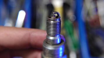 A detailed close-up image featuring a hand holding a worn spark plug against a blurred background of mechanical tools and equipment. video