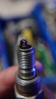 A hand holding a used spark plug, showcasing signs of wear and carbon buildup from engine use video
