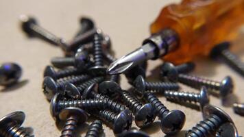 Metal screws scattered near a screwdriver on a wooden surface, representing tools for repair or construction. The sharp details of the screws highlight precision and craftsmanship. video