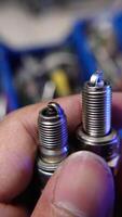 A hand holds both a new and a used spark plug side by side, clearly highlighting the significant differences in condition and wear. video