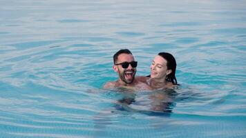 Young man and woman relaxing in a swimming pool, laughing and having fun. Concept joy, vacation and carefree lifestyle. video