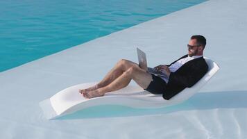 Man using laptop on a poolside lounger video