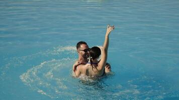 Very happy couple in sunglasses enjoying each other in a swimming pool, man holding woman in his arms, both smiling and relaxed. Concept vacation, travel, relaxation. video