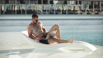 bonito jovem homem usando uma computador portátil de a piscina, desfrutando a verão atmosfera. conceito controlo remoto trabalhar, liberdade e relaxamento video