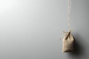 Small Burlap Sack Hanging from a Twine String Against a Gray Background. This image is ideal for minimalist designs and concepts related to simplicity and rustic charm. photo