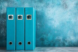 Teal Office Folders Against a Textured Blue Background. Three lever-arch files provide a clean and organized aesthetic. photo
