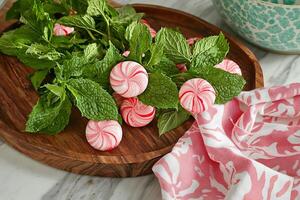 Peppermint Candies and Fresh Mint Sprigs on a Wooden Tray. A close-up image perfect for food blogs, culinary websites, and holiday-themed projects. photo