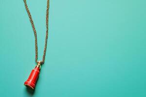 Red Perfume Bottle Pendant on Gold Chain Against Teal Background. A stylish image perfect for fashion, beauty, or luxury branding projects. photo