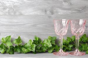 Elegant Pink Wine Glasses with Greenery on Rustic Wooden Background. A beautiful and stylish image perfect for wedding invitations, restaurant menus, or home decor websites. photo