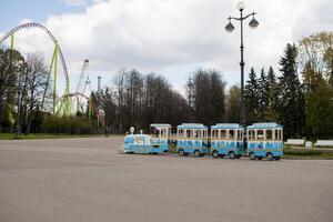 Colorful Tourist Train Waiting Near Amusement Park Rides on a Cloudy Day in Spring photo