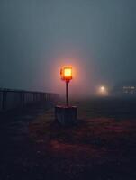 Blinking Warning Light Illuminates Foggy Landscape Near Distant Buildings at Dusk photo