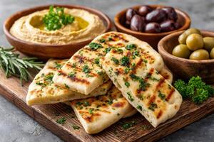 Grilled pita bread with hummus, green and black olives, and fresh herbs on wooden board photo