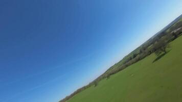 Low altitude FPV drone flight above green agricultural fields England UK video