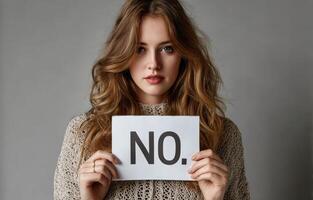 Woman holding sign saying NO in front of her face against a neutral background photo