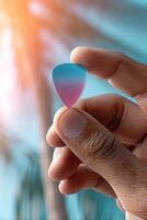 Guitar pick held in hand against colorful background with palm trees providing vibrant atmosphere photo