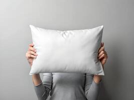 Woman's Hands Holding a White Pillow in Front of Her Face Against a Grey Background photo