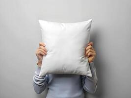 Person Hiding Face Behind White Pillow Against Gray Background photo