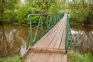 Wooden Bridge Over a Peaceful Stream Surrounded by Greenery in a Serene Countryside Setting During Springtime photo