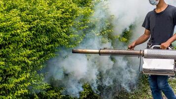 A man with a mask and a backpack spraying a bush with smoke photo