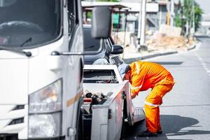 A man in an orange uniform is fixing a flatbed truck photo