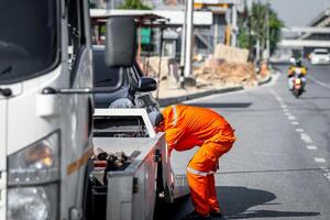 A man in an orange uniform is fixing a tow truck photo
