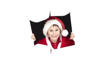 Child Santa Claus looks out of a hole in paper. The boy in Christmas rejoices. New Year's surprise. Christmas holiday concept photo
