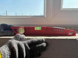 A red bubble level stands under a window in a new building. Measuring the window sill level. photo