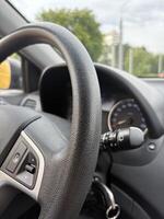 A vertical photo of a car steering wheel without hands while driving in the city.