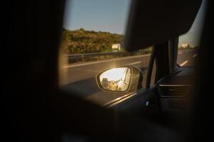 Reflections of a Road Trip Along the Highway at Sunset With Sunbeams Illuminating the Car Mirror photo