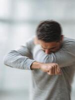 Male Individual Sneezing Into His Elbow in a Blurred Indoor Setting, Promoting Hygiene Awareness photo