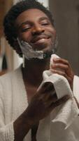 African American man shaving beard foamy gel in bathroom bearded guy wiping foam with towel shaven bristle male in mirror touching smooth skin shave prepare face care hygiene procedure cosmetic beauty video