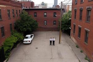 Two men standing in a parking lot next to a car photo