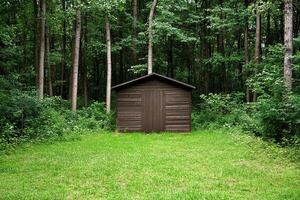A small shed sits in the middle of a green field photo