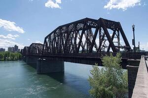 A train bridge crossing over a river with a city in the background photo