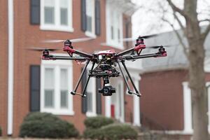 A large black and red drone flying over a house photo