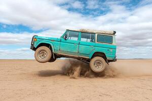 A blue jeep is jumping over a dirt field photo