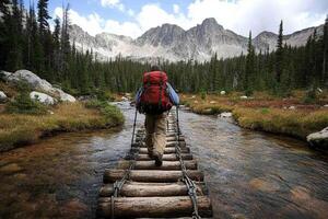 A man with a backpack crossing a wooden bridge over a stream photo