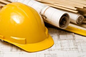 A hard hat and construction plans on top of a table photo