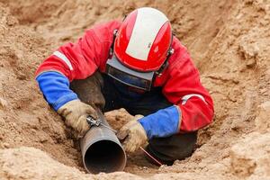 A man in a red helmet and red shirt is fixing a pipe photo