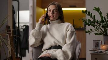 Positive excited Caucasian woman at home evening talking mobile phone call smartphone cellphone speaking friendship conversation happy female indoor gesturing emotions satisfied girl homeowner smiling video