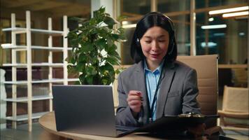 Asian Korean Chinese Japanese business woman businesswoman employer manager writing notes to do list working laptop computer online office female girl in headphones talking call meet with client video