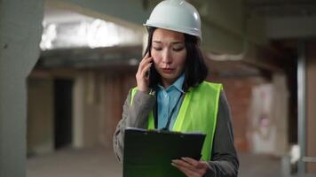 Emotional stressed Asian Korean woman builder talking mobile phone smartphone holding building plan project Chinese Japanese female discuss argue construction problem mistake engineer business girl video