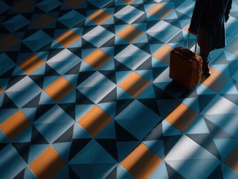 Person pulls tan suitcase across tiled floor with sunlight photo