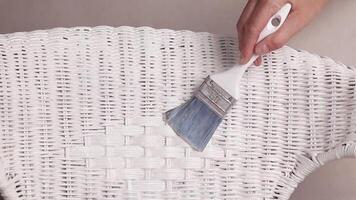 The hand holds a brush and paints with white paint or covers rattan with furniture varnish. Close up video