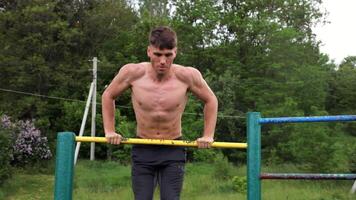 Hardy shirtlss sportsman doing push ups on horizontal bar at nature. Strong and muscular guy training at sports ground. Young athletic guy exercising outdoor. Concept of active and healthy lifestyle video
