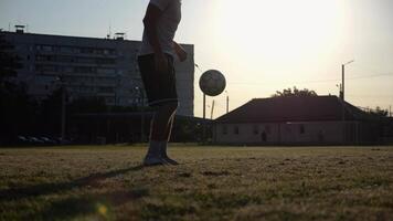 Professional footballer jugglin soccer ball on stadium at sunset. Young man kicking ball at green field. Sportsman practicing tricks at meadow with sunlight at background. Freestyle football concept video