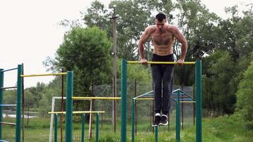 Hardy shirtless sportsman doi push ups on horizontal bar at nature. Strong and muscular guy training at sports ground. Young athletic guy exercising outdoor. Concept of active and healthy lifestyle video