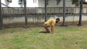 Man practicing yoga outdoors performing crow pose on green grass with palm trees in the background. video