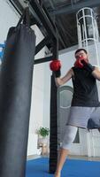 Man with boxing gloves training on punching bag indoors video