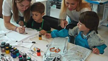 Young teachers at art school teach young children how to decorate and create unique denim clothes. They teach them how to craft these clothes in way that creates unique style. video